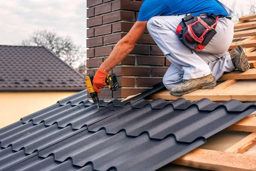 man installing metal roofing material on roof near chimney