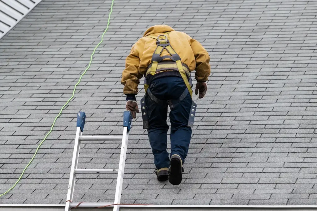 House during day with gray color Single Family Home and construction man in yellow uniform walking on roof shingles and ladder during repair; roof depreciation